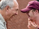 An older man and young man with Downs Syndrome smiling at each other.