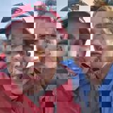 A man and a woman. the man is grinning at the camera and the woman is pouting a kiss. 